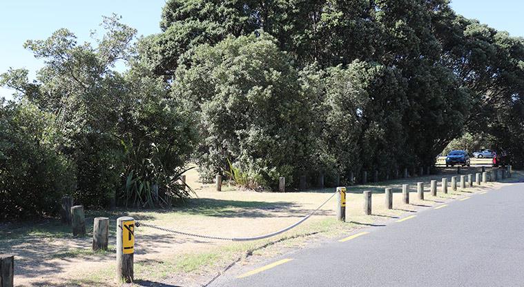 Long Bay Regional Park - Bookable site three entrance with a chain, bollards and trees in the background.