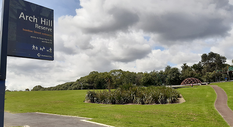 Arch Hill Scenic Reserve - Sign at the entrance to the park with open space, sports field, paths, and the playground in the background. Photo credit: T Hodder.