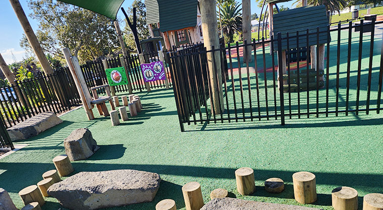 David Lange Park - A section of the junior play area showing the balance logs, low rocks for climbing on, interactive play boards on the fence and the junior play module in the background.