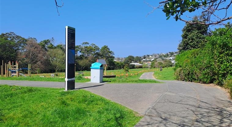 Whenua-roa / D'Oyly Reserve - Flat walking path with trees on right side and grassed area along with sign board on left side.