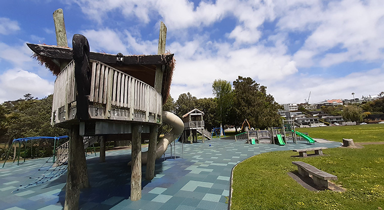 Ōrākei Domain - Side view of the one of the raised play huts with the rest of the playground, seats, open space and trees.