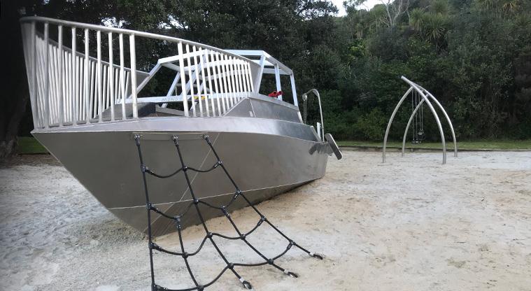 Tin Boat Reserve - Tin boat with a rope net up the front and a set of swings in the background.