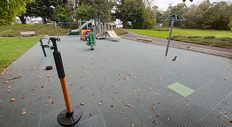 Waiatarua Reserve - Large area of rubber play surface with playground equipment, and surrounded by open grassed area and trees.